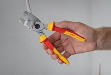 Une personne utilise une pince coupante isolée pour couper un câble électrique épais.