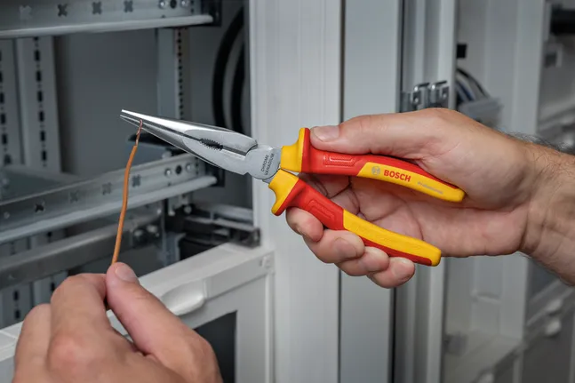 Une personne utilise une pince isolée pour plier un fil électrique lors de travaux dans un tableau électrique.