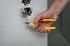 Une personne coupe un fil électrique avec une pince isolée à proximité de fils dénudés.