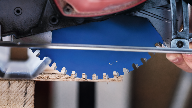 Gros plan sur la lame d'une scie circulaire en train de couper du bois.