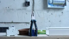 Une pince posée verticalement sur un établi, à côté de composants et de câbles électriques.