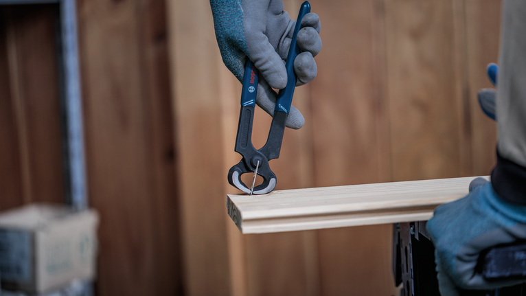 Une personne portant un équipement de sécurité utilise une pince coupante pour arracher un clou du bois.