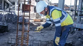 Une personne portant un équipement de sécurité fixe des barres d'armature à l'aide d'une pince sur un chantier de construction.