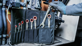 Une personne portant un équipement de sécurité choisit une clé dans une trousse à outils près de la machine.