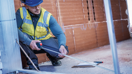 Une personne portant un équipement de sécurité utilise un outil de mesure numérique sur un chantier de construction.