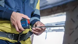 Une personne portant un équipement de sécurité utilise un mètre ruban sur un chantier de construction.