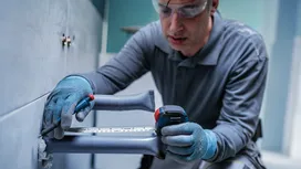 Une personne portant un équipement de sécurité mesure et marque un mur carrelé en céramique à l'aide d'un ruban à mesurer.