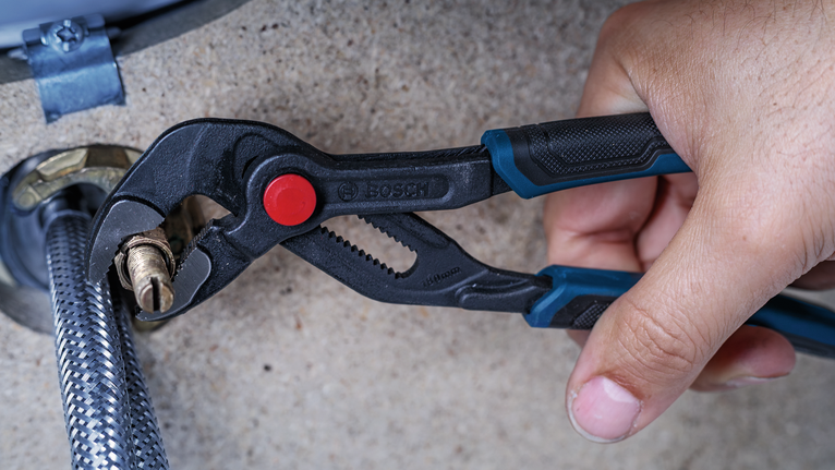 Une personne utilise une pince pour serrer un raccord en laiton sur un tuyau d'arrosage flexible.