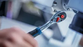Une personne utilise une clé à cliquet pour serrer un boulon sur une machine métallique.