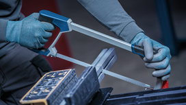 Une personne portant un équipement de sécurité coupe du métal avec une scie à métaux dans un atelier.