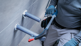 Une personne portant un équipement de sécurité coupe un tuyau avec une scie à métaux.