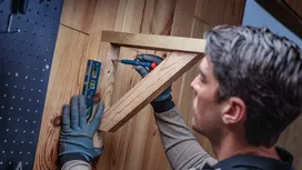 La personne portant un équipement de sécurité utilise un tournevis et un niveau à bulle pour aligner un support en bois.