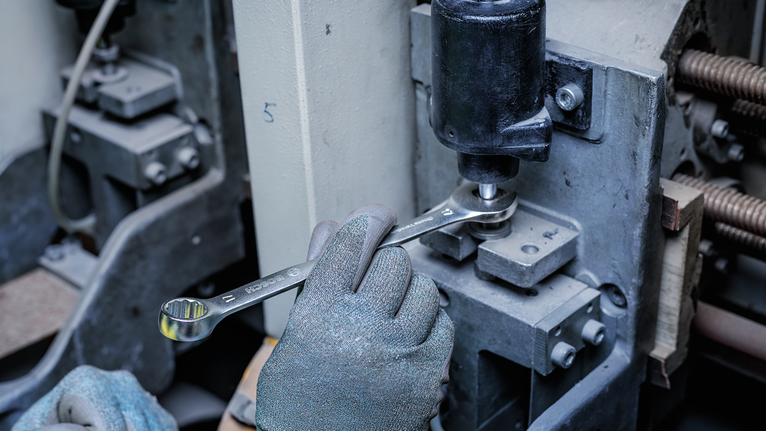 Une personne portant un équipement de sécurité utilise une clé pour serrer un boulon sur une machine industrielle.