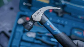 Une personne tient un marteau à griffes au-dessus d'une boîte à outils contenant divers outils.