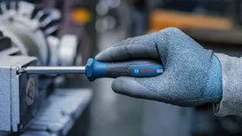 Une personne portant un équipement de sécurité serre une pièce de machine à l'aide d'un tournevis.