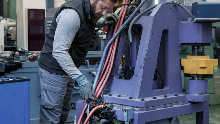 Une personne portant un équipement de sécurité utilise un outil électrique pour régler une machine dans un atelier industriel.