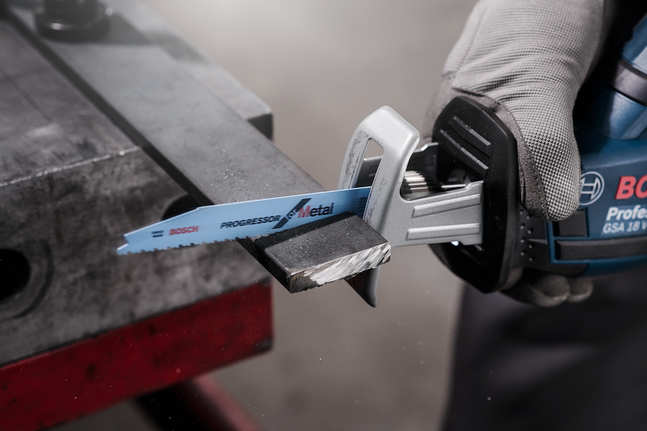 A worker wearing safety equipment cuts a metal bar using a reciprocating saw.