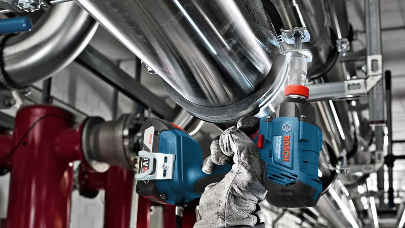 A person wearing safety equipment uses a power tool to tighten a pipe bracket.