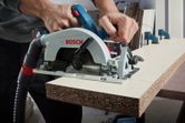 A person uses a cordless circular saw to cut particle board.
