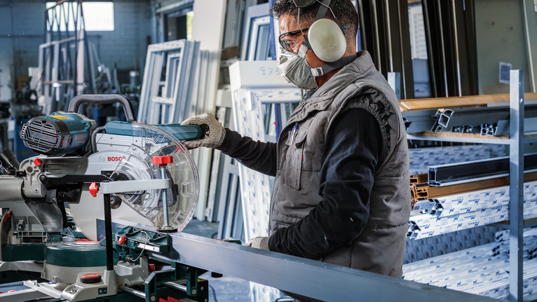 Person wearing safety equipment cuts a metal profile with a miter saw.