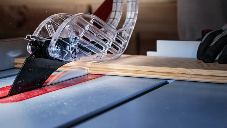 Person wearing safety equipment guides wood through a table saw blade in a workshop.
