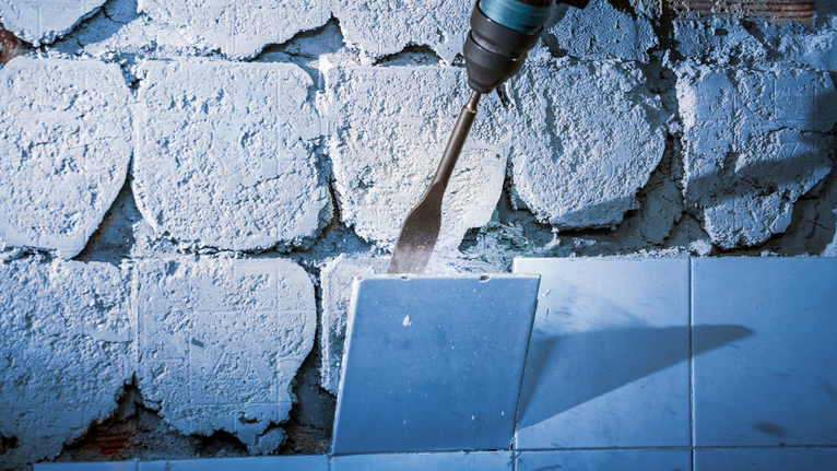 A power tool removes wall tiles with a flat chisel bit.