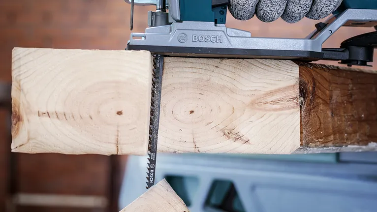 A power saw cuts through a wooden beam in a workshop.