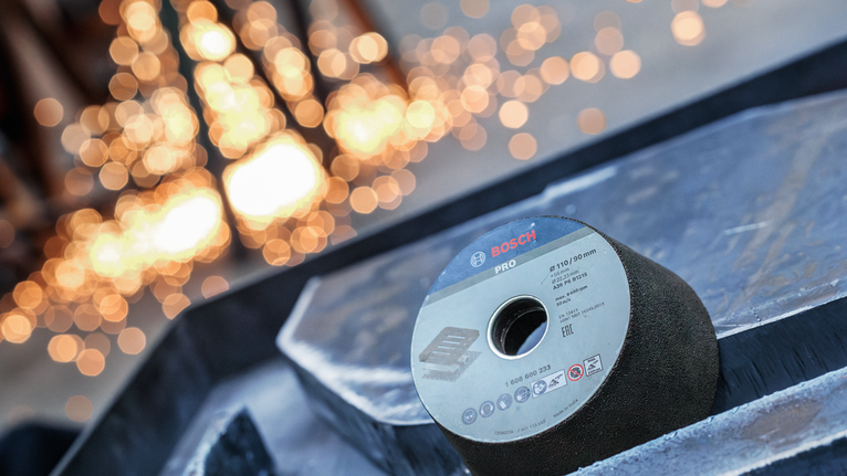 Grinding wheel placed on a metallic surface with blurred workshop lights in the background.