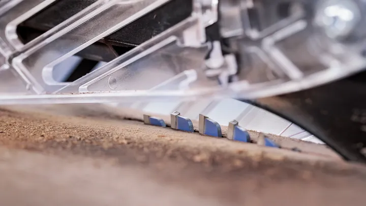 Circular saw blade cutting through a wooden board under a clear protective guard.