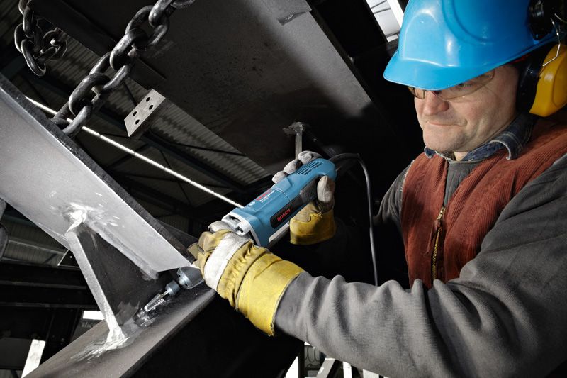 Uma pessoa que usa equipamento de segurança utiliza uma retificadora reta numa viga de aço.