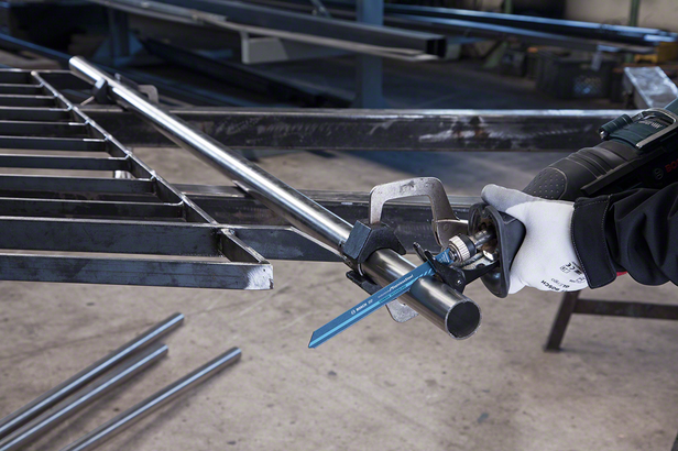 Trabalhador que utiliza equipamento de segurança utiliza uma serra alternativa para cortar um cano de metal.