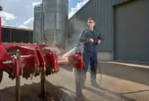 Uma pessoa que usa equipamento de segurança utiliza uma lavadora de alta pressão para limpar máquinas agrícolas vermelhas.