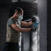 Uma pessoa que utiliza equipamento de segurança tritura uma parede de betão com uma rebarbadora angular.