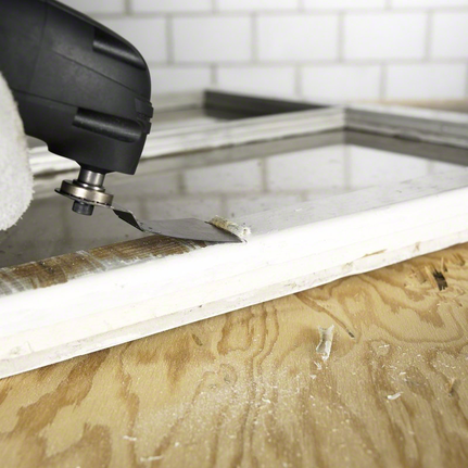 Uma pessoa que utilize equipamento de segurança utiliza uma ferramenta multifuncional para remover material da moldura de uma janela.