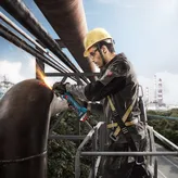 Uma pessoa que utiliza equipamento de segurança tritura um grande tubo de metal com uma rebarbadora.