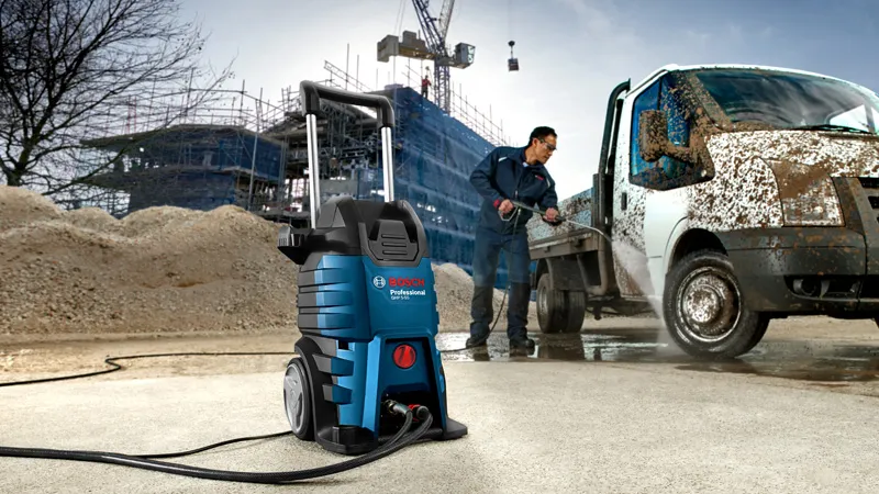 Uma pessoa que usa equipamento de segurança utiliza uma lavadora de alta pressão para limpar uma carrinha de trabalho lamacenta.