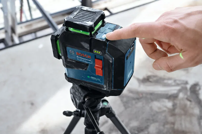 Uma pessoa opera uma ferramenta de nivelamento a laser montada num tripé num estaleiro de construção.