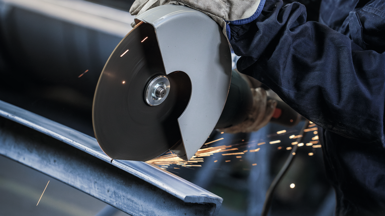 Uma pessoa que usa equipamento de segurança corta metal com uma rebarbadora, e as faíscas voam.