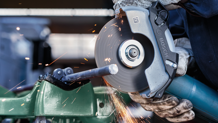 Uma pessoa que usa equipamento de segurança corta uma barra de metal com uma serra circular, produzindo faíscas.