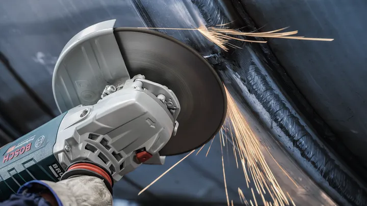 Uma pessoa que usa equipamento de segurança tritura metal, produzindo faíscas.