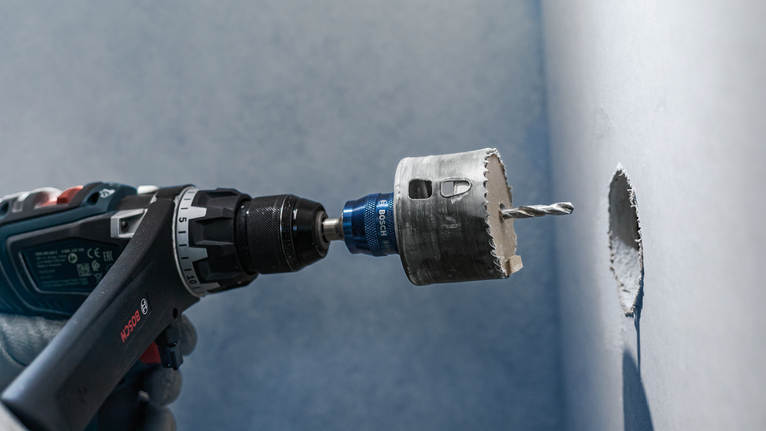 Uma pessoa que use equipamento de segurança faz um furo circular na parede.