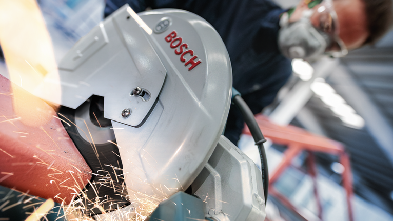 Pessoa que usa equipamento de segurança a cortar metal com uma serra circular, com faíscas a voar.