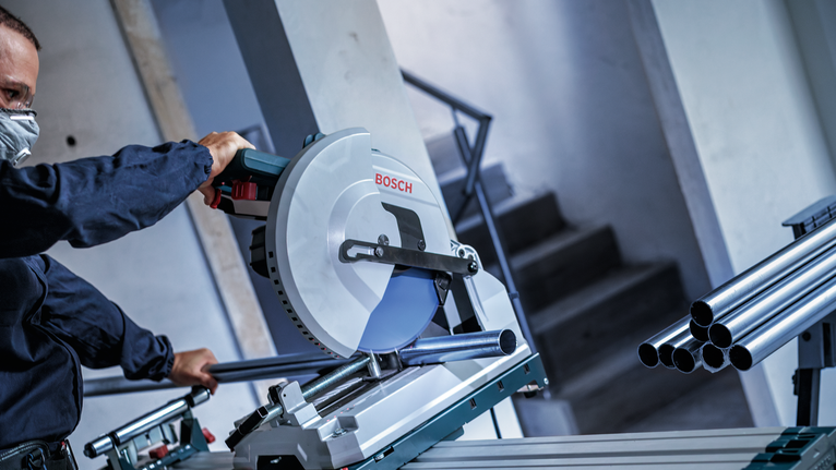 Pessoa que usa equipamento de segurança a cortar tubos de metal com uma serra circular.