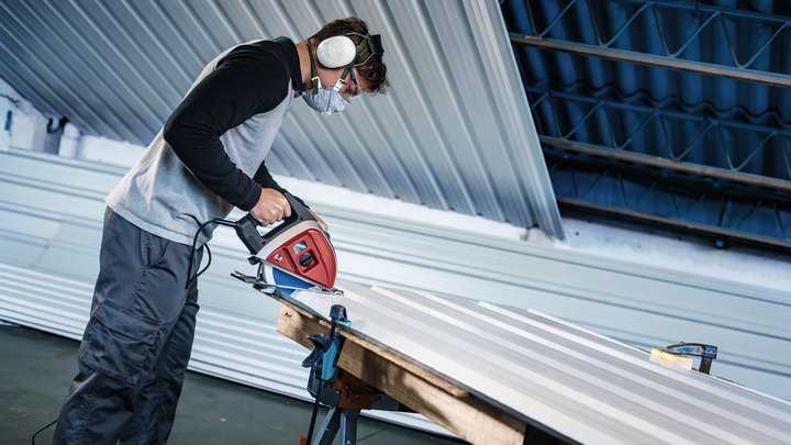 Uma pessoa que usa equipamento de segurança corta chapas metálicas com uma serra elétrica.