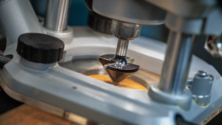 Broca de tupia a entalhar uma superfície de madeira sobre uma mesa de oficina.