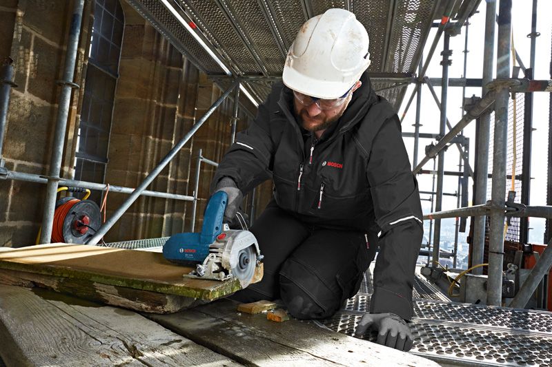 Una persona que usa equipo de seguridad corta madera con un cortador de baldosas de diamante en un andamio.