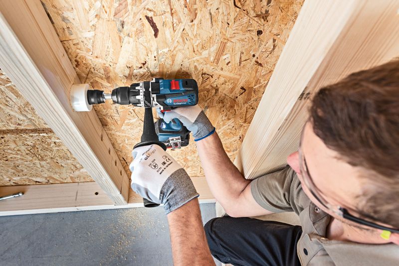 Una persona que usa equipo de seguridad perfora una sierra de corona en un panel de madera.