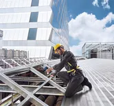 Una persona que usa equipo de seguridad perfora un marco de metal en una obra en construcción en la azotea.