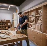 Una persona que usa equipo de seguridad perfora madera en un banco de trabajo en un taller de carpintería.
