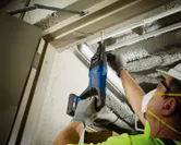 Una persona que usa equipo de seguridad perfora un techo de hormigón utilizando un martillo perforador inalámbrico.